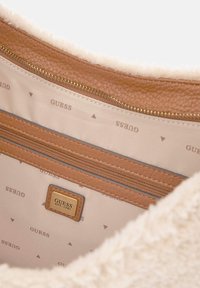 Hnědý interiér tašky z umělé kůže s kapsou na zip, krémovým plyšovým podšívkou a opakujícím se vzorem loga v světle béžové.