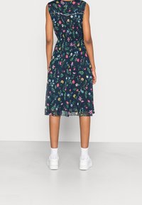 Floral knee-length dress in dark navy fabric with various colorful flowers. Features a gathered waist and sleeveless design, paired with white sneakers.