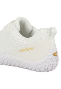 White athletic shoe with a textured mesh upper, featuring a gold logo and a white, patterned rubber sole. Rounded heel with a pull tab.