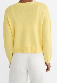 Yellow knitted sweater with a loose fit, ribbed neckline and hem, and dropped shoulders. Worn with white high-waisted pants.