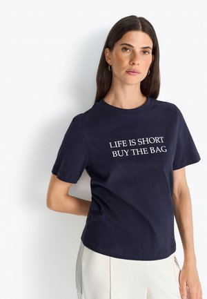 T-shirt en coton bleu marine avec des manches courtes et un col rond. Graphisme texte "LA VIE EST COURTE, ACHETEZ LE SAC" en blanc sur la poitrine.
