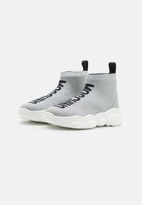 Graue gestrickte Ankle Boots mit einer strukturierten Oberfläche, versehen mit schwarzen Logo-Akzenten und einer weißen, klobigen Sohle mit abgerundeten Details.