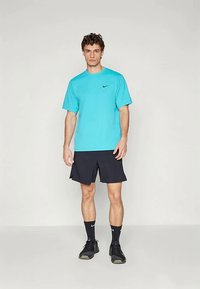 Camiseta turquesa de Nike combinada con pantalones cortos negros. El material parece ligero, el diseño es simple, con un pequeño logo en el pecho. Zapatillas deportivas negras.