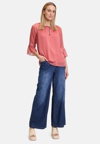 Blusa rosa con maniche a tre quarti e scollatura a forma di chiave, abbinata a jeans in denim blu a gamba larga e sandali con plateau beige.