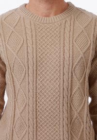 Pull en tricot beige avec un motif texturé à cable et en losanges. Encolure et manches côtelées, en matière de laine douce.