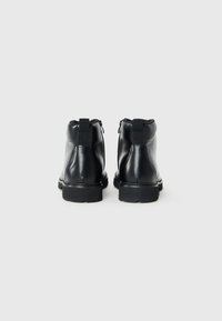 Botas de tobillo de cuero negro con un acabado suave, punta redondeada y suela gruesa. Incluye cremalleras laterales y lengüetas para facilitar el uso.