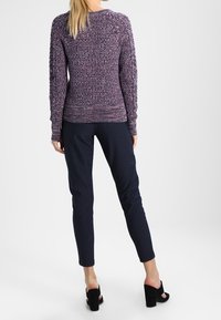 Maglione viola a maglia con motivo testurizzato, abbinato a pantaloni a righe blu navy. Maniche e cintura presentano dettagli a costine. Scarpe nere con tacco alto.