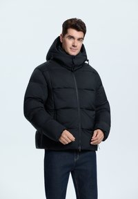 Schwarze Steppjacke mit hohem Kragen, ausgestattet mit einem durchgehenden Reißverschluss, Seitentaschen und einem gesteppten Design. Die Textur wirkt glatt und isoliert.