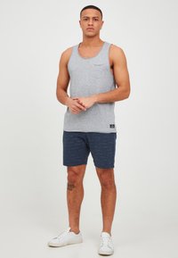 Grå bomullstanktopp med en ficka, kombinerad med marinblåa shorts med strukturerat mönster. Vita sneakers fulländar outfiten.