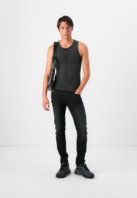 Top de tirantes de mezclilla negra con costuras visibles, combinado con jeans skinny negros. La modelo lleva zapatillas y un bolso negro tipo bandolera.