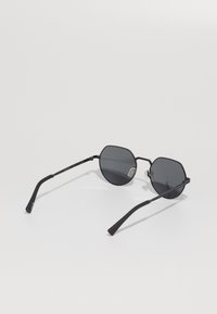 Ochelari de soare negri, în formă de octagon, cu lentile întunecate, rame subțiri din metal și brațe drepte. Au tampoane pentru nas pentru un confort sporit.