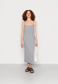 Vestido maxi cinzento canelado com alças finas e pala de botões. A modelo segura uma mala branca e usa sandálias pretas. Design simples e ajustado.