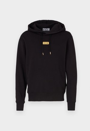 Black hoodie with a front pocket, drawstrings, and gold metal accents. Features a gold logo patch on the chest. Made of soft fabric.