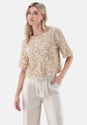 Kurz geschnittenes Oberteil mit kurzen Ärmeln in hellbeige, verziert mit verstreuten goldenen und schwarzen Pailletten. Kombiniert mit hellgrauen, hoch taillierten, plissierten Hosen.