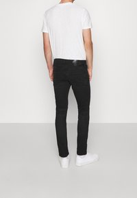 Černé skinny džíny s hladkou strukturou, pětipocketovým designem, minimálním prošíváním a koženou nášivkou na zadním pásku. Bílé tenisky.