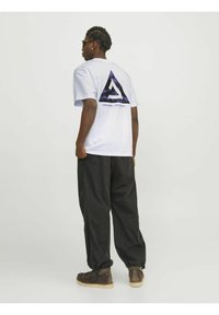 T-shirt bianco a maniche corte con un design a triangolo viola e nero sul retro, abbinato a pantaloni neri e stivali marroni.