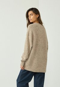 Beige strikket sweater med ribbet tekstur, lange ærmer og en afslappet pasform. Spraglet mønster tilføjer detalje. Sammen med bredbenede mørk denim bukser.