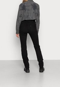 Jeans skinny negros y una camisa de tie-dye gris oscuro con cuello de botón, mostrada desde la parte de atrás con textura suave y diseño ajustado.