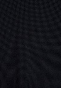 Tumma sininen ribbineulos, jossa on teksturoitu pinta. Materiaali näyttää pehmeältä ja joustavalta, mikä tekee siitä ihanteellisen vartalonmyötäisiin vaatteisiin.