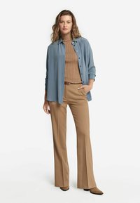 Camicia in jeans azzurro chiaro, dolcevita marrone a coste, pantaloni beige a zampa d'elefante e stivaletti marroni con tacco. Tessuto liscio, vestibilità rilassata.