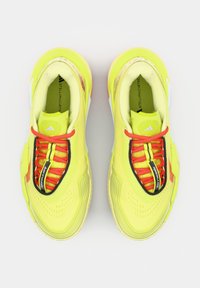 Felle gele hardloopschoenen met rode veters, zwarte afwerking en "Stella McCartney" branding binnenin het hielgedeelte.