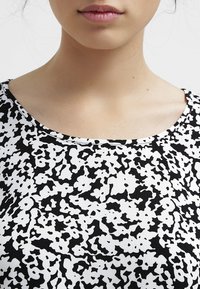 Svart och vit mönstrad tyg med en abstrakt design, med rund halsringning och en mjuk textur. Närbild av plagget.