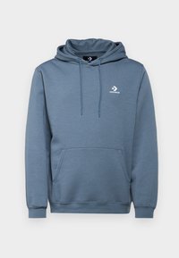 Sudadera gris de tela suave, con un bolsillo canguro, capucha ajustable con cordón y un logo blanco en el pecho.