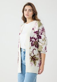 Strickjacke in Creme mit floralen Mustern in Pink, Lila und Grün. Hat lange Ärmel und eine lockere Passform. Offenes Frontdesign.