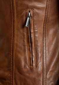 Bruine leren jas close-up, met een ritszak met een zilveren trekker en zichtbare stiksels op een gestructureerd oppervlak.