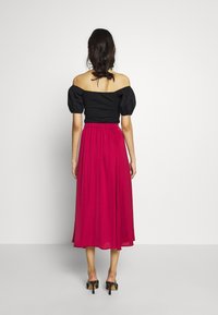 Zwarte off-shoulder top met pofmouwen, gecombineerd met een vloeiende roze midi-rok, elastische tailleband en zwarte hoge sandalen.
