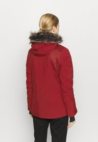 Czerwona kurtka ocieplana z futrzanym kapturem, o gładkim wykończeniu i dopasowanym kroju. Tył ma prosty design.
