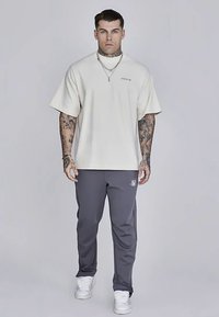 Kremowy, oversize'owy t-shirt z krótkim rękawem, zestawiony z szarymi, zwężanymi spodniami dresowymi z logo. Całość uzupełniają białe sneakersy.