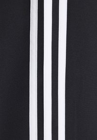 Gros plan sur un tissu noir avec trois bandes blanches verticales cousues en parallèle au centre.