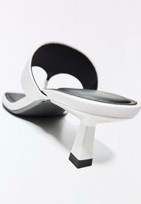 Hvid højhælet mule-sko med sort polstret fodseng og firkantet hæl, vinklet visning på hvid baggrund.