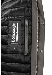 Giubbotto imbottito con un interno trapuntato nero e un esterno grigio. Include una tasca con zip e una patch con il logo sul davanti. Taglia L.