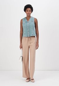 Jeans uten ermer med v-hals og frontknapper, kombinert med beige stripete vide bukser og lyse sko.