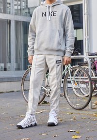 Grå hoodie med svart "NIKE"-logotyp, vita träningsbyxor med en logotypmärke och vita sneakers med röda bokstäver "AIR".