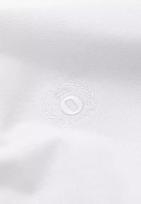 Tela blanca con un tejido texturizado, que presenta un logo bordado de una corona y unaurel con la letra "O" en el centro.
