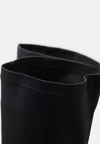 Bottes noires à cheville avec un tissu lisse et souple et un bord supérieur replié. Des coutures visibles le long des bords ajoutent du détail au design.