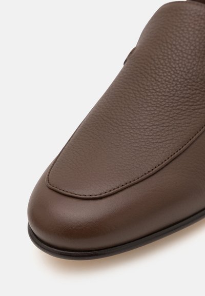 Chaussure slip-on en cuir marron, avec une texture lisse, un bout arrondi et un subtil détail de couture le long du bord supérieur.