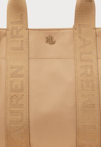 Sac fourre-tout beige avec de larges anses tissées embossées du texte "Lauren" et un petit logo métallique RLL au centre en haut.