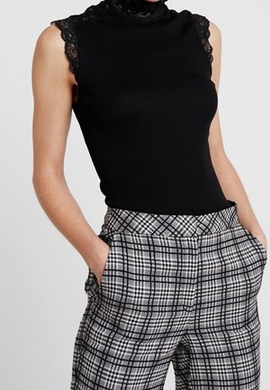 Top negro sin mangas con textura acanalada y detalles de encaje en los hombros, combinado con pantalones de cuadros en blanco y negro de cintura alta, con bolsillos laterales.