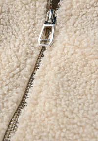 Tessuto in pile beige con un aspetto texturizzato e soffice, caratterizzato da un dettaglio con zip argentata lungo un bordo.
