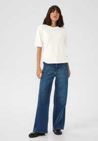 Haut blanc à manches courtes associé à un jean en denim bleu moyen à jambes larges et des chaussures à plateforme noires. Design simple avec une coupe décontractée.
