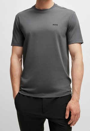 Mand iført en simpel mørkegrå T-shirt med korte ærmer med "BOSS"-logo på brystet, kombineret med sorte bukser.