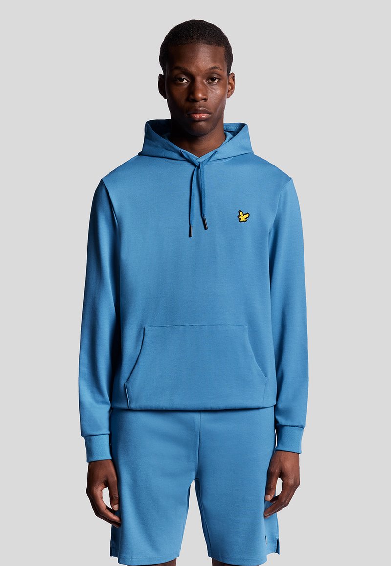 Felpa blu con tasca frontale, cappuccio con cordino e dettaglio del logo giallo. Abbinata a pantaloni corti blu coordinati in tessuto morbido.