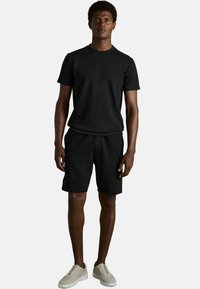 Camiseta de manga corta negra y pantalones cortos a juego, confeccionados en una tela suave. Completado con zapatillas de color claro, el conjunto tiene un ajuste relajado.