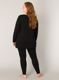 Zwarte lange mouwen top met een relaxed fit en afgeronde zoom, gecombineerd met zwarte leggings. Glad textuur, minimaal ontwerp en geen zichtbare patronen.