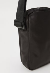 Černá crossbody taška z nylonu, obdélníkového tvaru, s nastavitelným popruhem a hladkým povrchem se zipovým uzavřením.