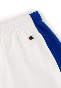 Weiße Sportshorts mit blauen seitlichen Einsätzen. Mit elastischem Bund, der mit genähten Details versehen ist, und einem kleinen schwarzen Logo in der Nähe des Bundes.